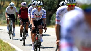 Photo of seven elite cyclists in uniforms biking down a road; most are in UAE uniforms